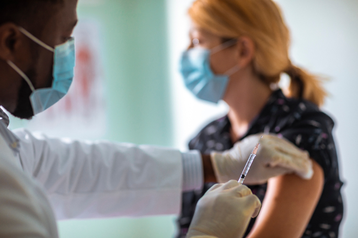 Doctor vaccinating a young woman in the arm while both wear masks