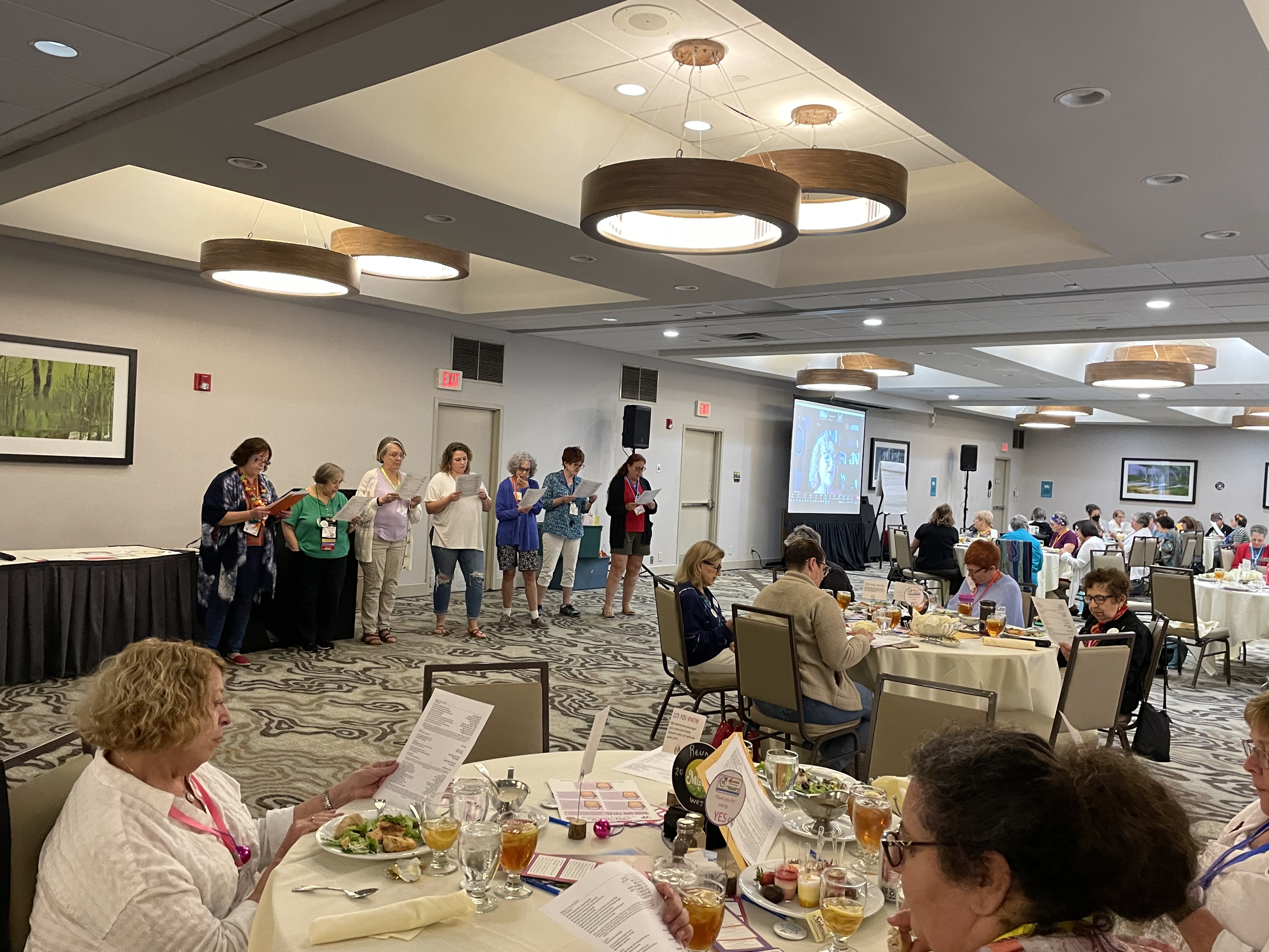 women sitting around tables and also standing in a room. 