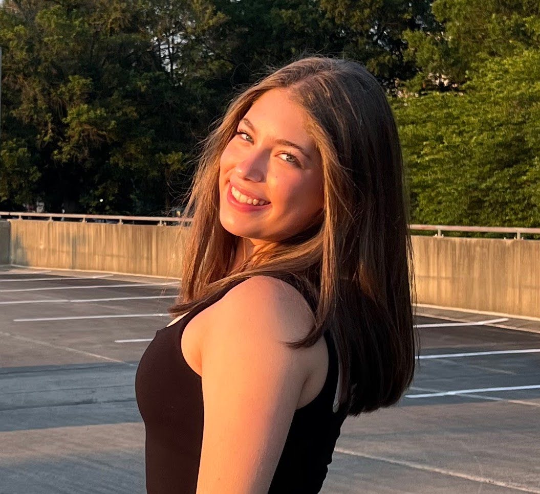 girl smiling over her shoulder with shoulder length brown hair in a black tank top