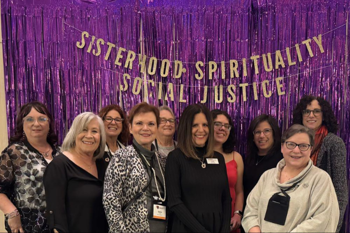 Members of WRJ Southeast District stand in front of purple tinsel wall with words "Sisterhood, Spirituality, Social Justice" in sparkly gold letters