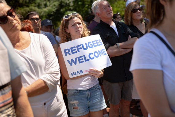 Protesters gathered, one holding a sign that says "refugees welcome"
