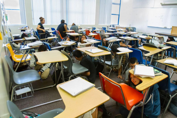 Photo of kids sitting under their desks inside of a classroom