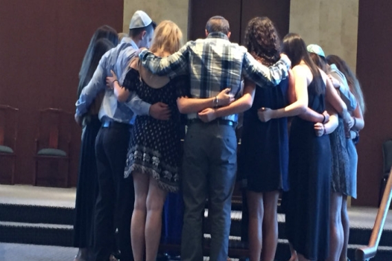 A circle of people with linked arms on the bima of a synagogue