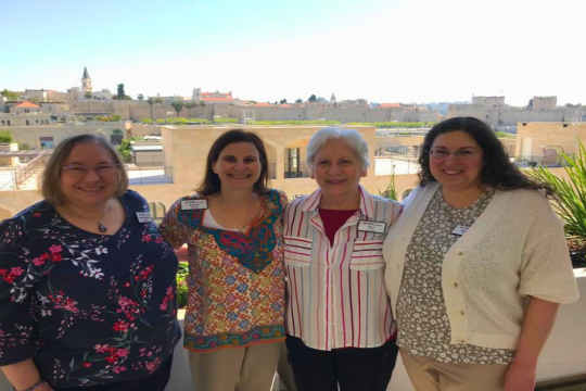 Four women stand together with an Israeli scenic background. 