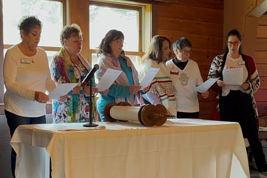 A group of women standing around a table looking at a Torah. 