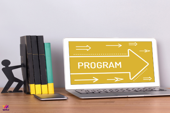 A figure-shaped bookend pushing a stack of book adjacent to a laptop with Program on its screen.