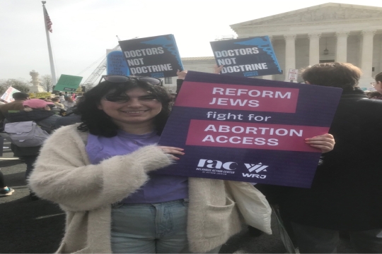 Rachel Landis holding a Reform Jews Fight For Abortion Access poster in front of the Supreme Court