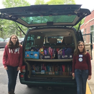 Women standing by a parked car filled with donations.
